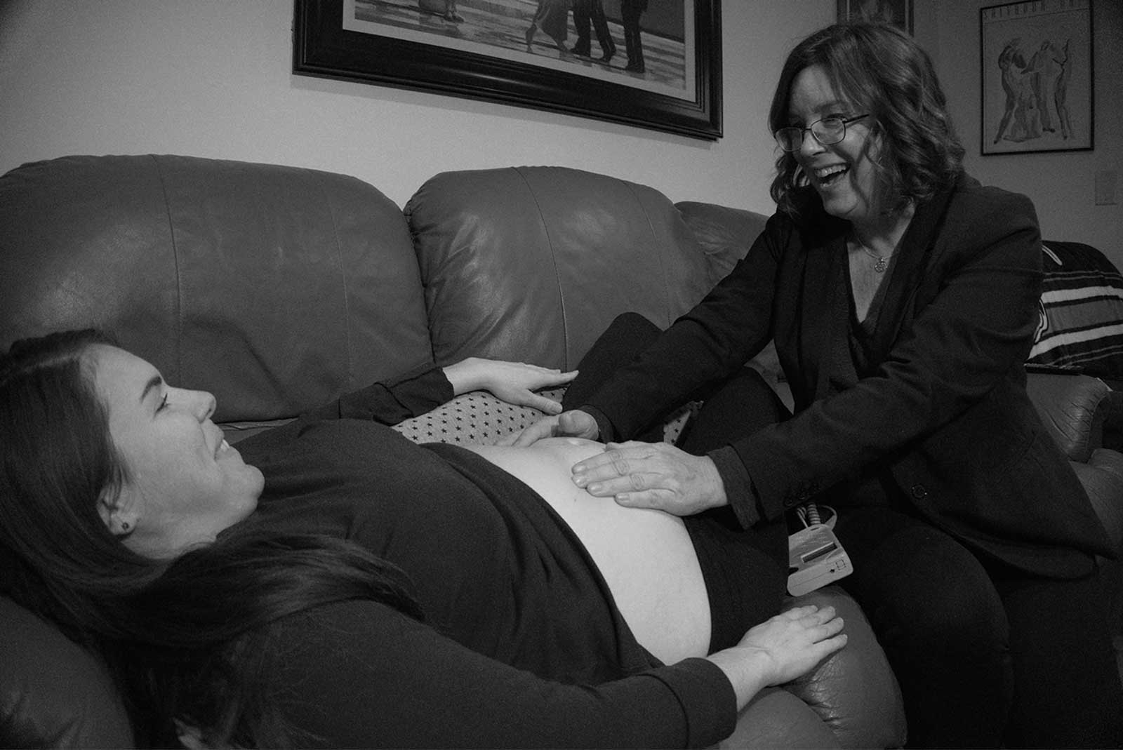 midwife with pregnant client sitting on couch hands on belly